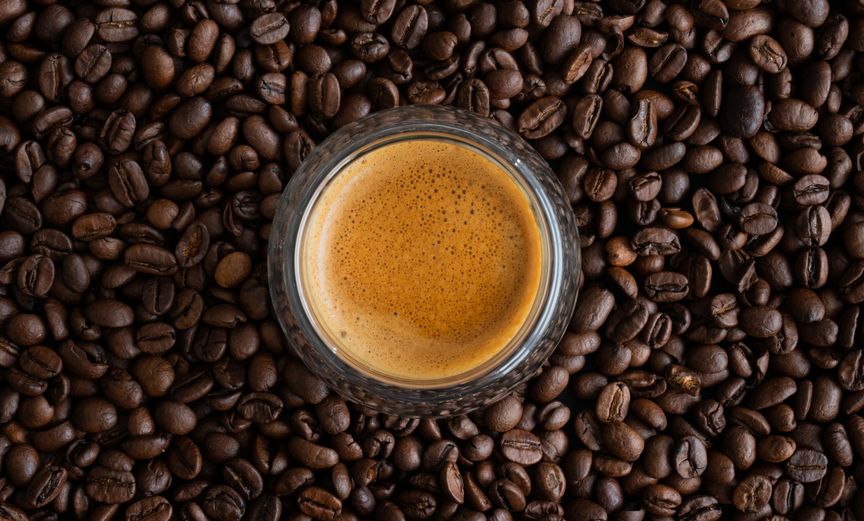 Espresso in einer transparenten Tasse, vor einem Hintergrund aus frischen Kaffeebohnen