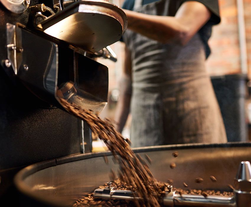 Mitarbeiter bedient den Zulauf an Kaffeebohnen zu der Trommel im Trommelröstverfahren